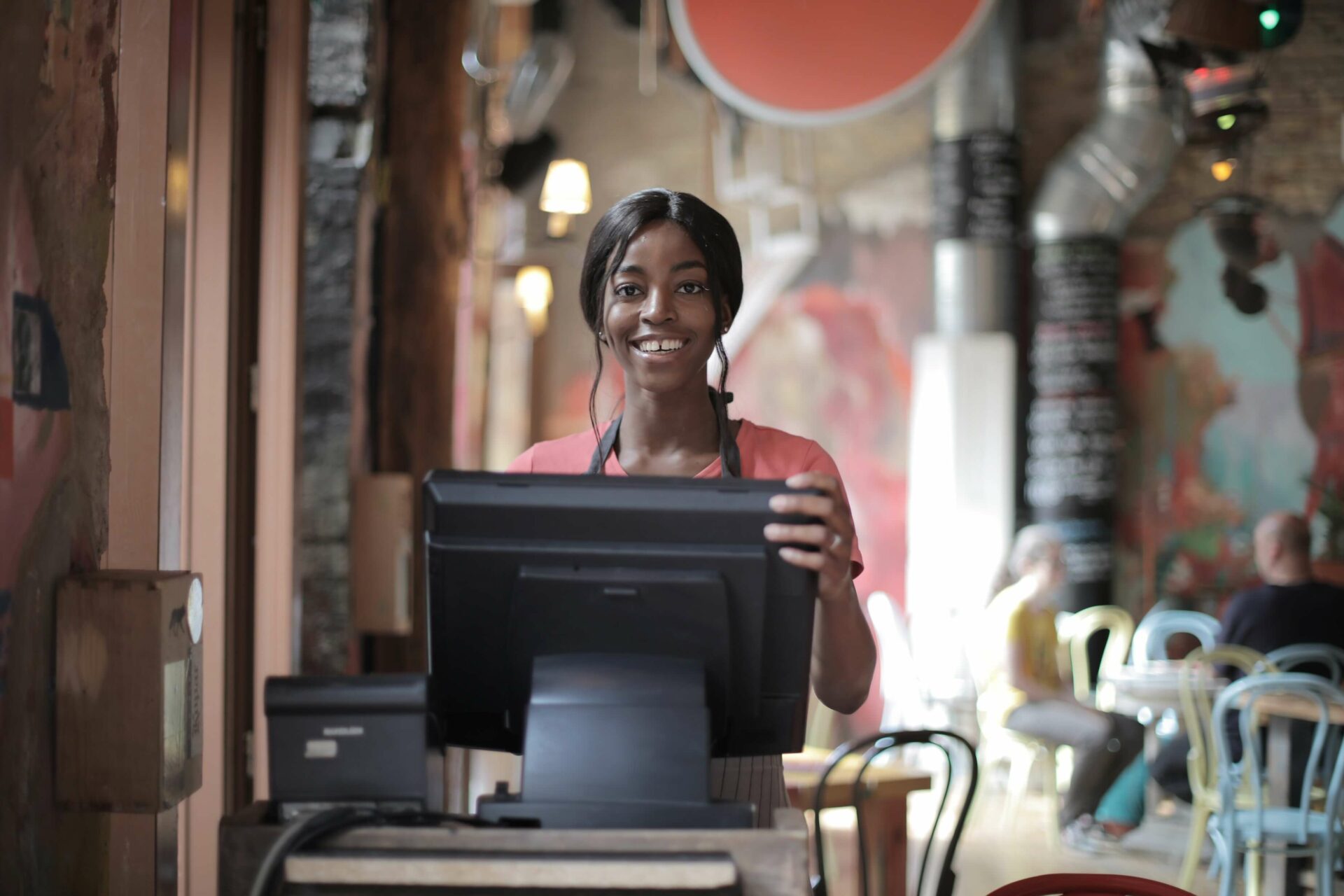 Smiling woman in coffee shop standing next to till