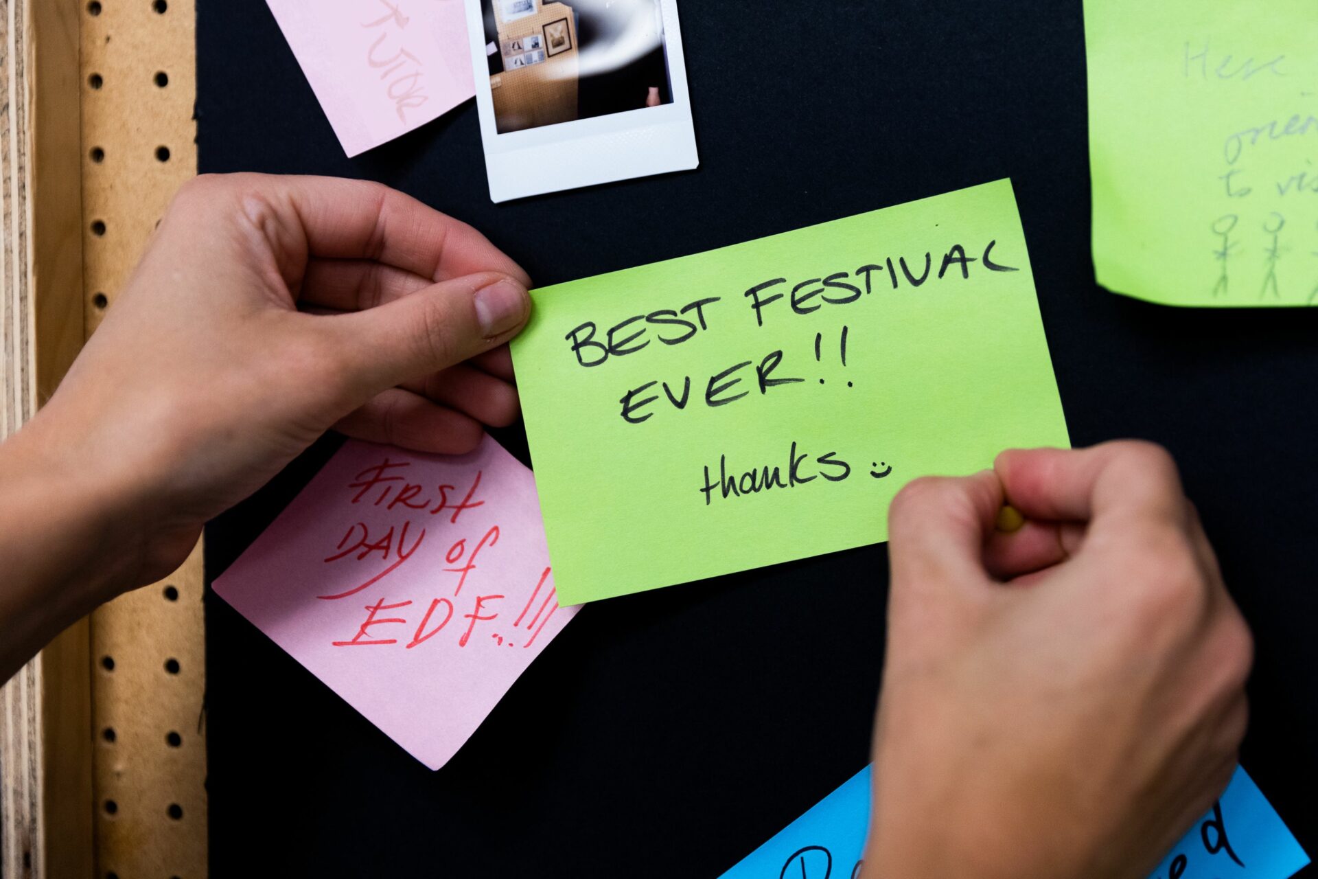 Hands pinning up green post-it which reads 'best festival ever'