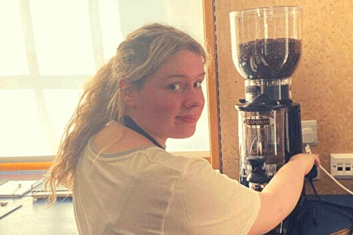 Woman in white top turning towards camera while using coffee machine
