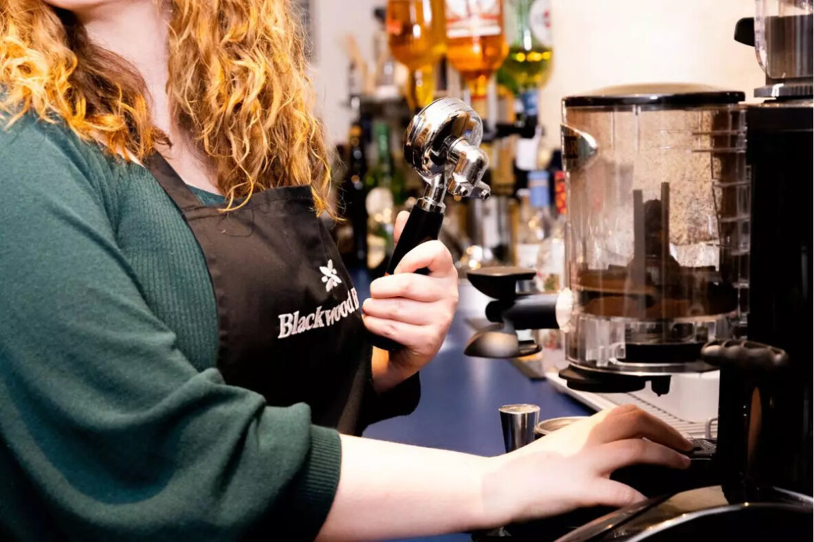 Women in green black apron using espresso machine to make coffee
