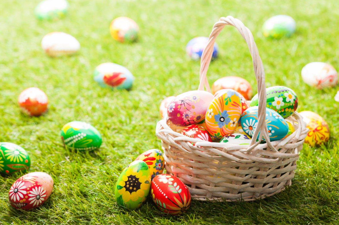 Easter egg hunt basket on grass with various decorated eggs scattered around