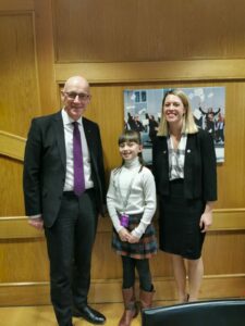 Niamdh Braid tsanding in the middle of John Swinney and Jenny Gulrith at the Scottish Parliament.