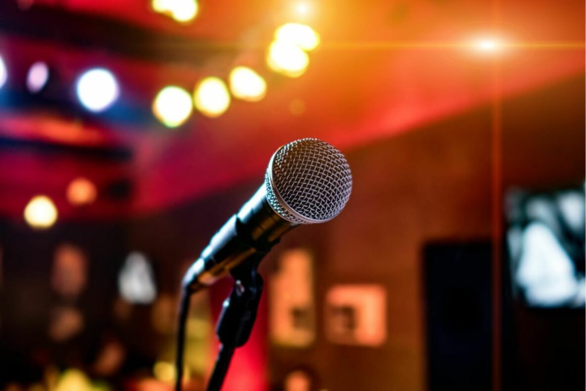 A microphone stand with a mic. Behind it are bright lights and people.